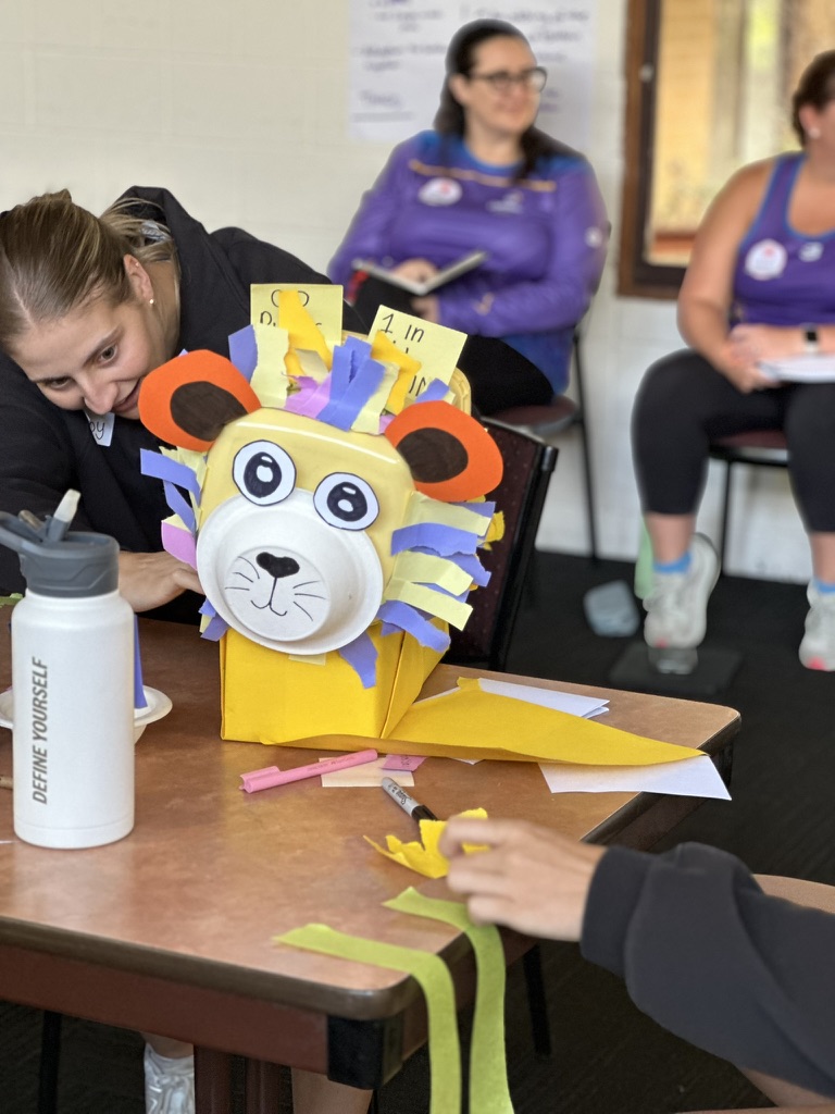 a young woman adds details to a handmade paper lion as part of a team building activity.