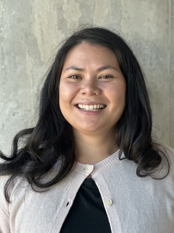 picture of Emily Farrell wearing a cream top and smiling the camera against a grey concrete background.