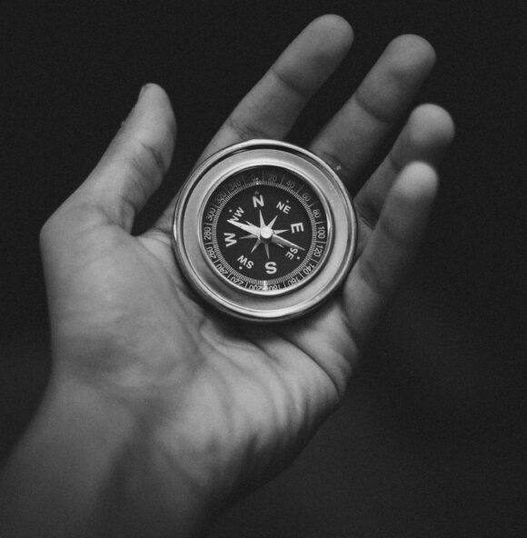 a black and white picture of an upturned hand holding a compass