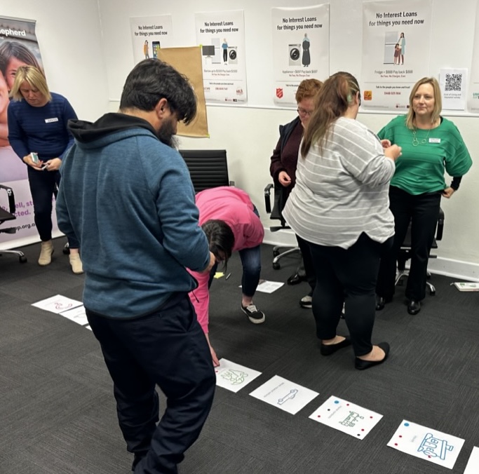 a group of people standing around a row of posters on the floor, looking thoughtful.