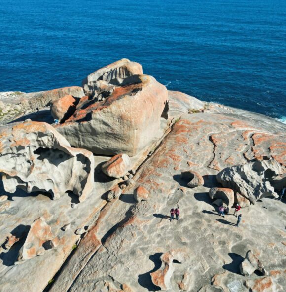 unusual grey and orange rock formations on a cliff top in front of a deep blue sea, viewed from above
