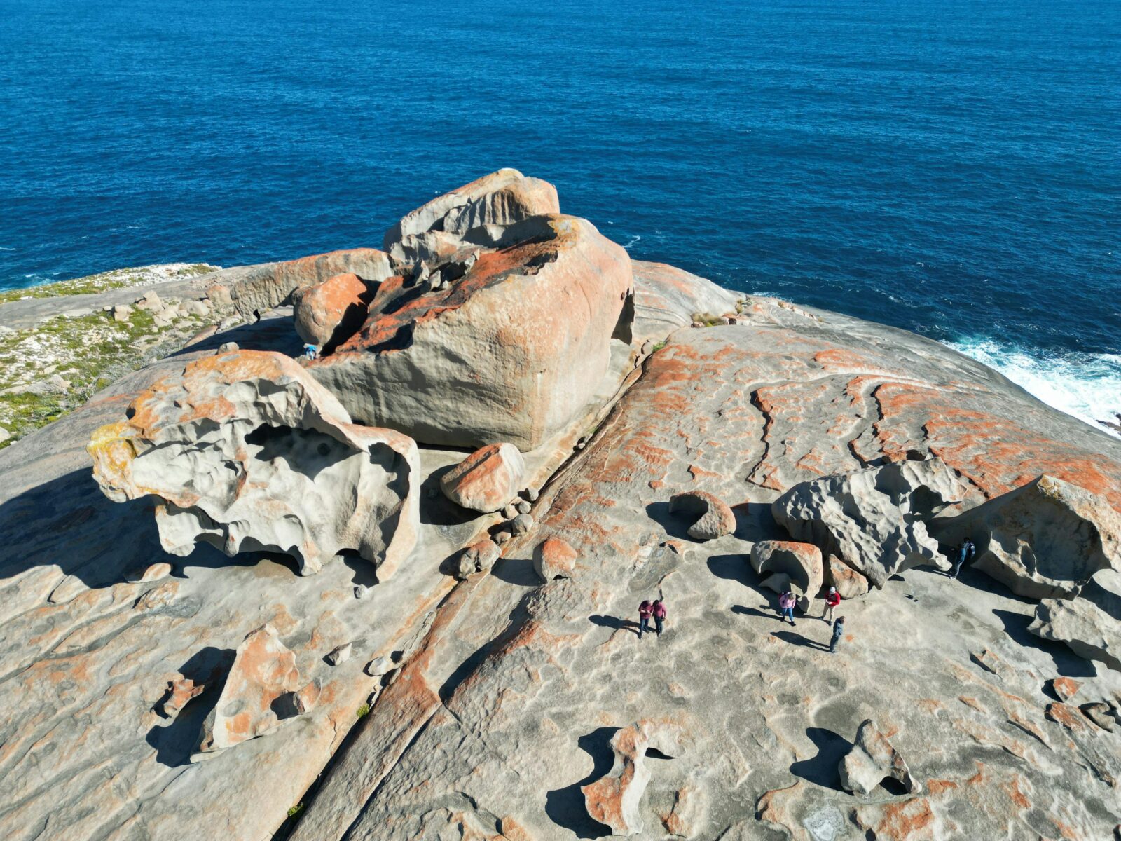 unusual grey and orange rock formations on a cliff top in front of a deep blue sea, viewed from above